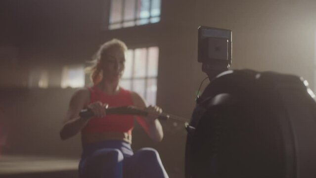 Fitness young woman using rowing machine in the gym crossfit training. Slow-motion shot