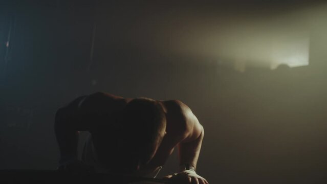 Athletic young man performing push ups on tyre, exercising at warehouse enjoying physical activity