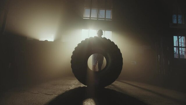 Front view of a strong muscular shirtless man flipping a heavy tire in slow-motion during his workout session