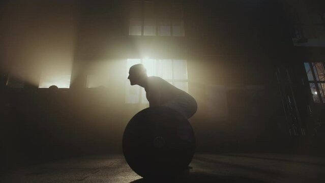 Full shot of a handsome powerlifter man with muscular body lifting a heavy barbell in gym. Side view, slow-motion