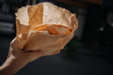 Hand holding cheese bread in a paper bag in morning sun.