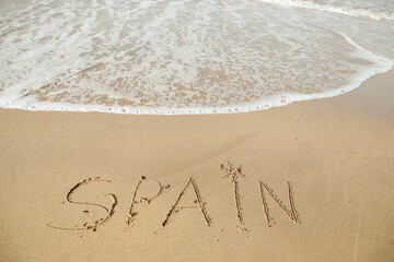 Spain lettering on the beach with wave and clear blue sea. 
