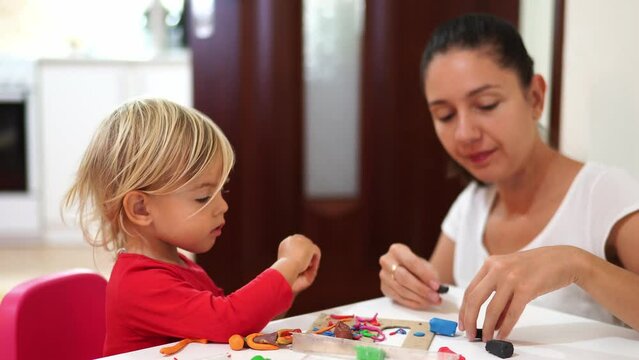 Mom teaches a little girl to sculpt crafts from plasticine at the table