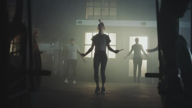 A group of people exercising together in abandoned warehouse. Group of five people doing jumping rope exercise and two men cycling on exercise bike