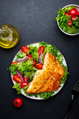 Fried cod fish with salad garnish from lettuce, cherry tomatoes and red onion with sesame seeds,...