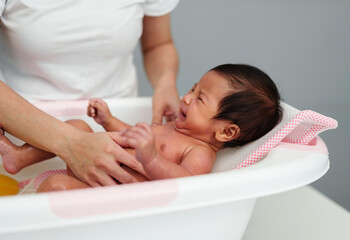 Fototapeta na wymiar mother give a bath with crying newborn baby in bathtub