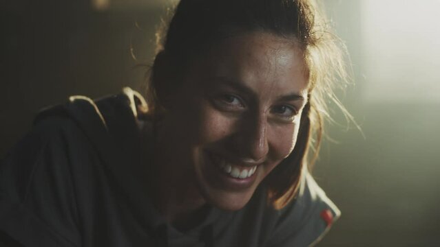 Portrait of beautiful young tired and sweaty woman looking at camera and smiling cheerfully in slow-motion. Sweat on her face