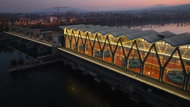 Colorful sky reflecting in the Rhine river with the illuminated turbine house of the hydro power plant in Birsfelden Switzerland. Drone dolley shot