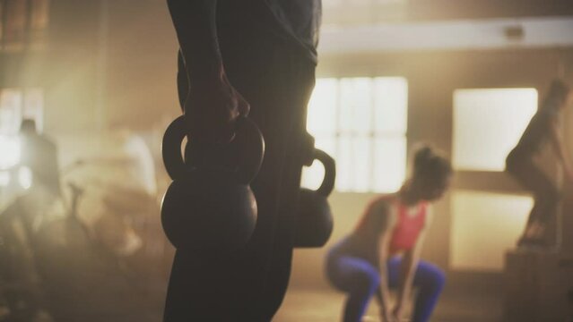 Young man in focus doing kettlebell exercise while group of friends working out together in the background