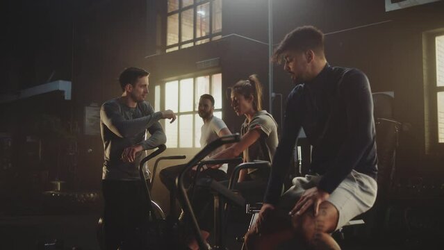 Group of male and female friends working out at gym with stationary bike while male trainer checking speed of stationary bike. Concept of health and fitness