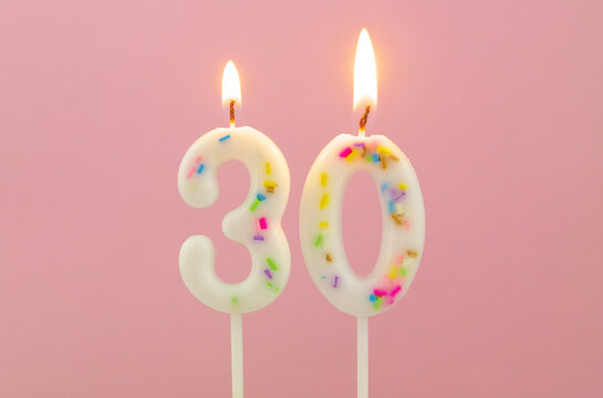 White decorated burning birthday candles on pink background, number 30