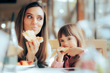 Hungry Mom and Daughter Having Pizza in a Restaurant. Happy family craving for fast food meal
