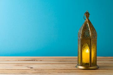 Lightened lantern on wooden table over blue background. Ramadan kareem holiday celebration concept