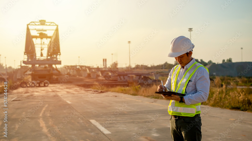 Poster asian engineer with hardhat using tablet pc computer inspecting and working at construction site