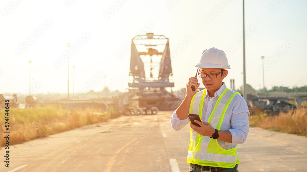 Poster engineer talking on walkie-talkie and using smart phone for working at construction site