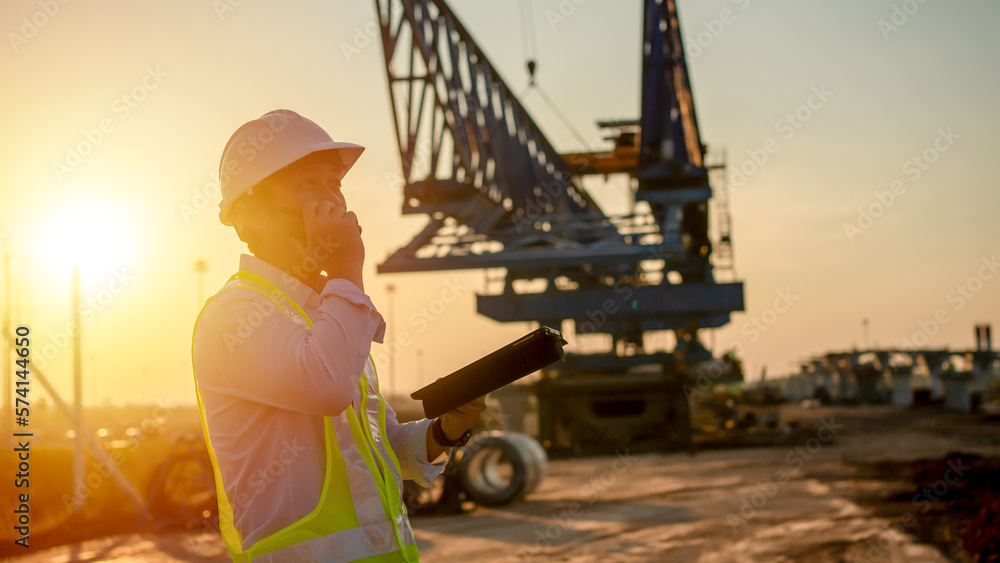Poster engineer talking on walkie-talkie and using smart phone for working at construction site