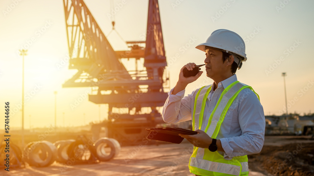 Poster engineer talking on walkie-talkie and using smart phone for working at construction site