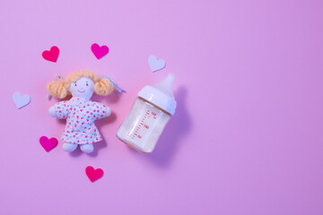 哺乳瓶と人形とハートのピンク背景の左寄りの写真 - obrazy, fototapety, plakaty