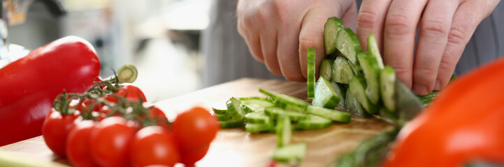 Green cucumbers are cut with knife in kitchen