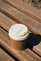 Eco recycling paper cup with coffee or tea on kraft paper on wooden table. Breakfast on the street in the park on bench. Take away coffee to go. Copy space for text. Disposable Cardboard