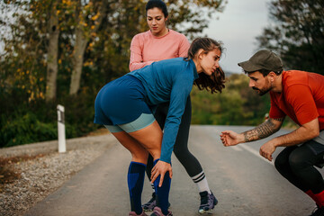 Obraz premium A woman feels pain in her leg during jogging. Calf muscle cramp. Friends helping her.