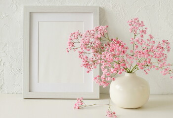 Portrait frame mockup with copy space for artwork, photo, painting, print presentation and beige  modern vase with pink flowers near white wall .Minimal scandinavian interior design.