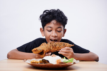 Asian boy enjoys fried fish and rice at lunch time