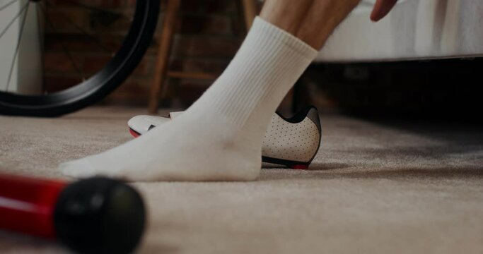 A man takes off his cycling shoes after training on an bike exercise at home, close-up of male legs, no face, side view. Cycling indoors