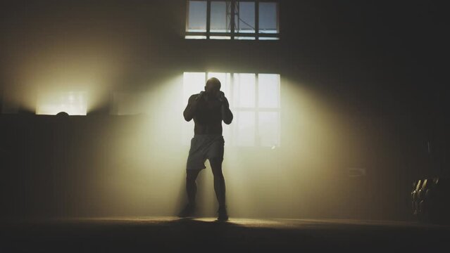 Extreme slow-motion shot of a muscular sportsman practice boxing with shadow in abandoned warehouse
