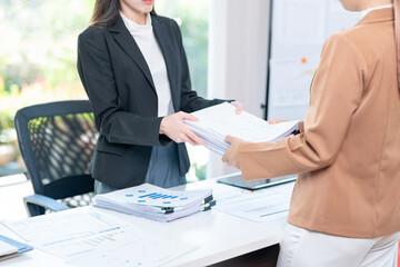 Two business women sharing documents in office modern corporate building. Female coworkers handling paperwork