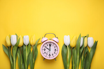 Pink alarm clock and beautiful tulips on yellow background, flat lay with space for text. Spring...