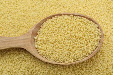 Spoon with raw couscous as background, top view