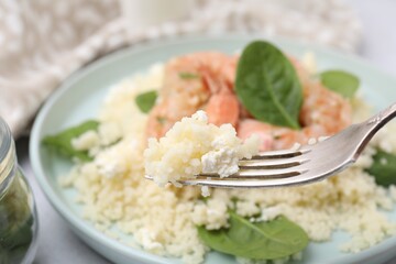Fork with delicious couscous over plate, closeup