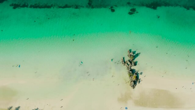 White Beach of Boracay and people swim at turquoise azure sea near Grotto Willy's Rock upon which stands the Virgin Mary Statue. Copy space for text. Summer and travel vacation concept.