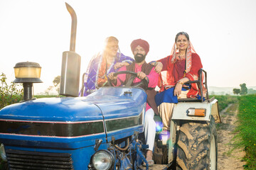 Rural indian punjab farmer family driving tractor at agriculture field outdoor. Culture of india....