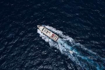 Obraz premium Big white boat moving faster diagonally top view. Large yacht in motion on dark water aerial view.