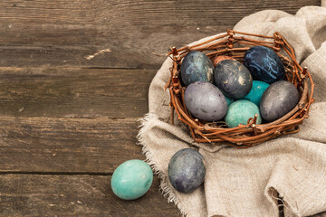 Easter eggs in wicker basket and blooming cherry on old wooden background. Festive greeting card