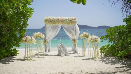 wedding setup flowers chairs. Wedding arch decorated ceremony beach. Marriage venue detail white ribbon with rose flower seaside outdoor. Tropical Palm tree island summer paradise.
