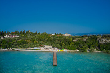 Wooden pier, turquoise water. Panoramic aerial view of Lido delle Bionde beach, Sirmione, Lake Garda, Italy.