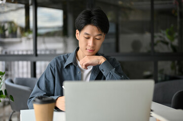 Smart and concentrated young Asian male college student remote working at the cafe