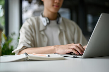 Focused Asian male college student typing on keyboard, browsing internet, using laptop