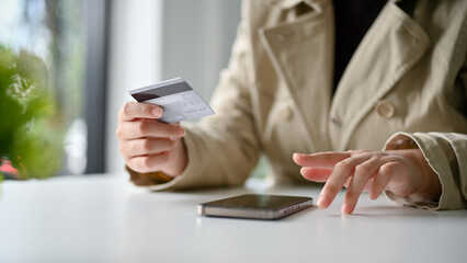 an Asian woman sits at the table using mobile banking app to transfer her money or paying bills.