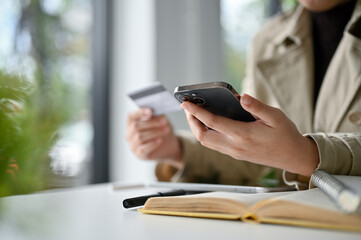 an Asian woman in the coffee shop and using her mobile phone to pay her online bills.
