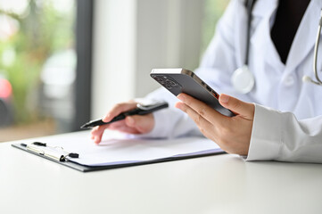 Fototapeta premium Cropped image of a professional Asian female doctor using her smartphone at her desk.