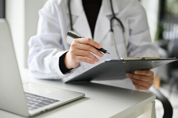 Professional Asian female doctor working at her desk in the office, reading medical cases