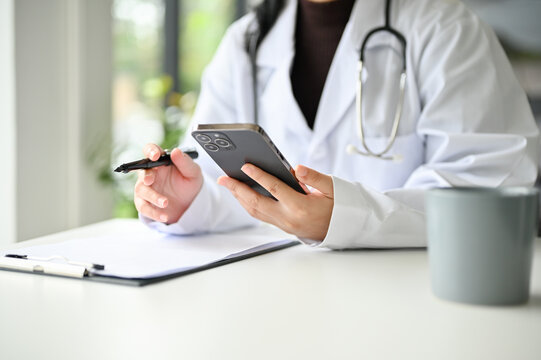 Cropped image of a smart Asian female doctor using her smartphone at her office desk.