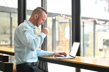 Side view of caucasian businessman drinking coffee and checking email on laptop computer