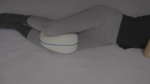 Woman lying down with an orthopedic pillow for her knees. Knee Ease.