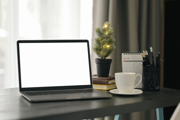 Home office desk with laptop, coffee cup, potted plant and calendar on black wooden table. Blank screen for advertisement