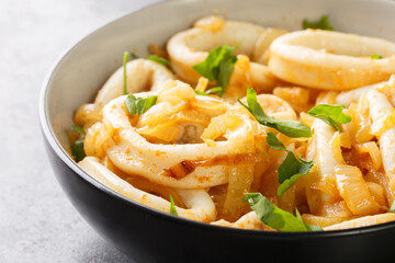Delicious stewed squid rings with caramelized onions in wine sauce close-up in a bowl on the table. Horizontal